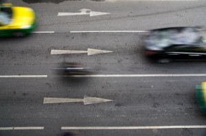 Overhead image of cars speeding by on a road with arrows pointing in the direction the cars are moving.