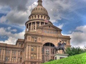 A majestic tan building with a statue of a man on a horse in front of it.