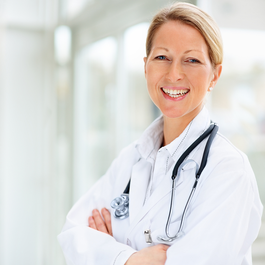 A woman with blonde hair smiling in a white doctors jacket with a stethoscope around her neck.