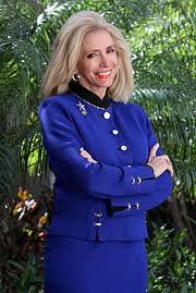 A woman in a purple suit with blonde hair nodding and smiling.