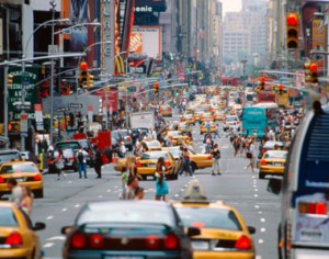 A crowded New York City street with people, cars, and yellow taxis everywhere.