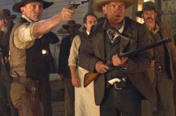 Two guys wearing cowboy hats; one holding a pistol and one holding a shotgun.