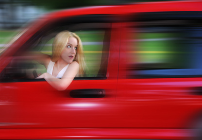 Woman driving a red car blurred because she is speeding.