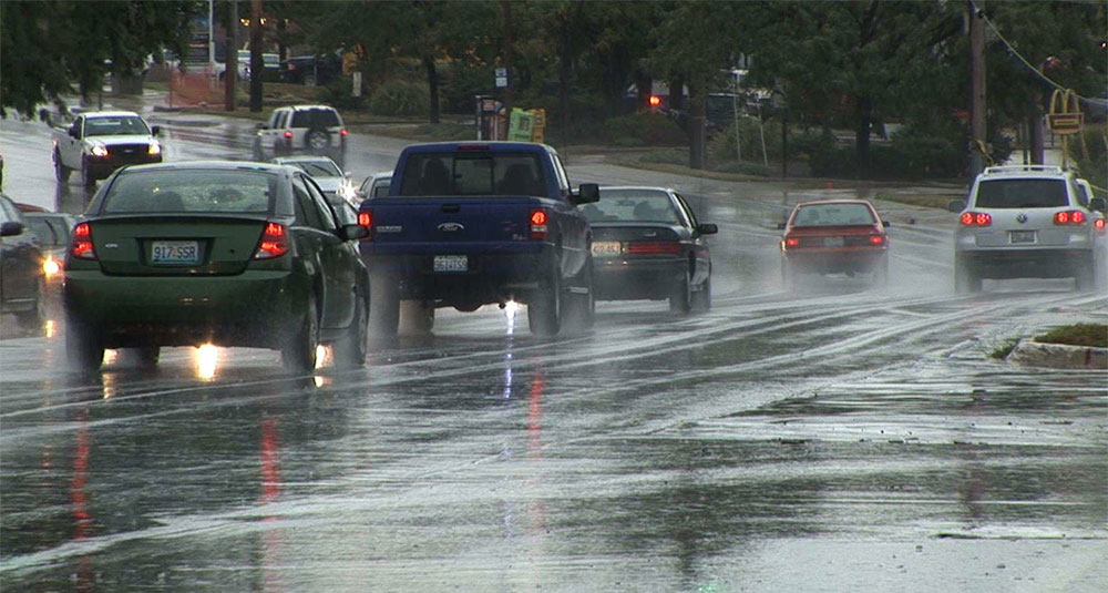 A number of cars all driving on a slick, slippery looking road.