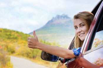 A woman driving a red car poking her head out the window and giving a thumbs up.