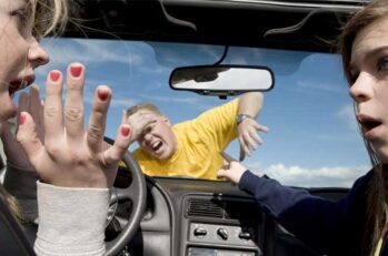 Two young female drivers looking at eachother as they hit a man in a yellow shirt holding his forehead.