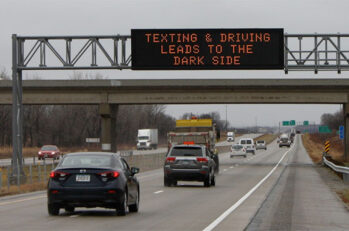 Cars on an interstate driving underneath a digital sign that says "Texting & Driving Leads to the Dark Side."