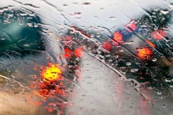 Up close image of rain on a window with traffic behind it.