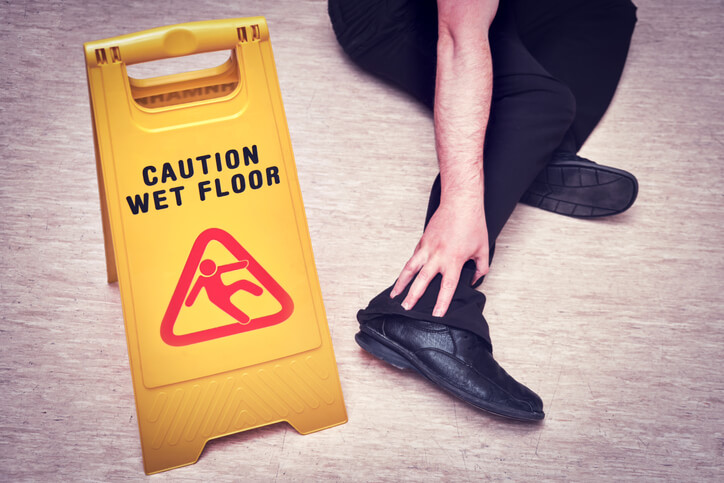 An accident occurs as a person falls and injures themselves on the wet floor. The sign on the plate with the text - caution wet floor
