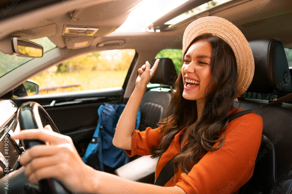 A happy woman drives down the road, ecstatic that she did the research, picked the best defensive driving course for her, and received her auto insurance discount.