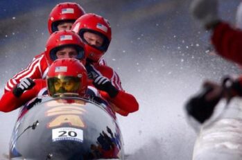 Four guys wearing red suits and helmets sitting in a bobsled.