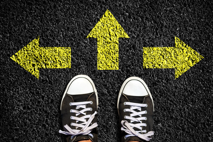 Sneakers on an asphalt road. Yellow arrows pointing in different directions. View from above. The concept of choosing the right path.