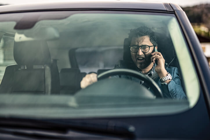 Angry businessman driving a car and having a phone discussion.