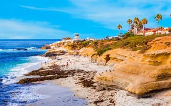 A beautiful beachfront with cliffs right near the water and people lounging in the distance.