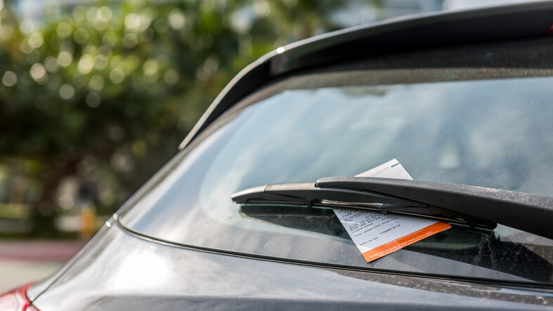 A parking ticket is left under a vehicle's windshield wiper.