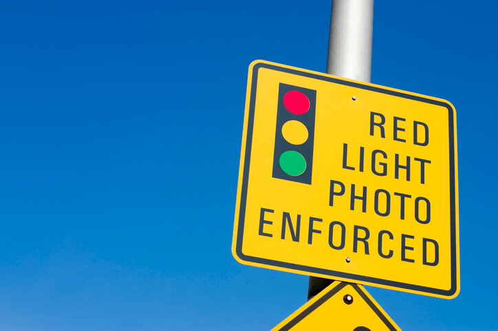 A sign hanging on a metal pole warns drivers of an intersection that has cameras enforcing red lights.