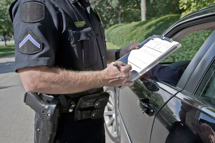 A police officer filling in a ticket by a pulled over car.