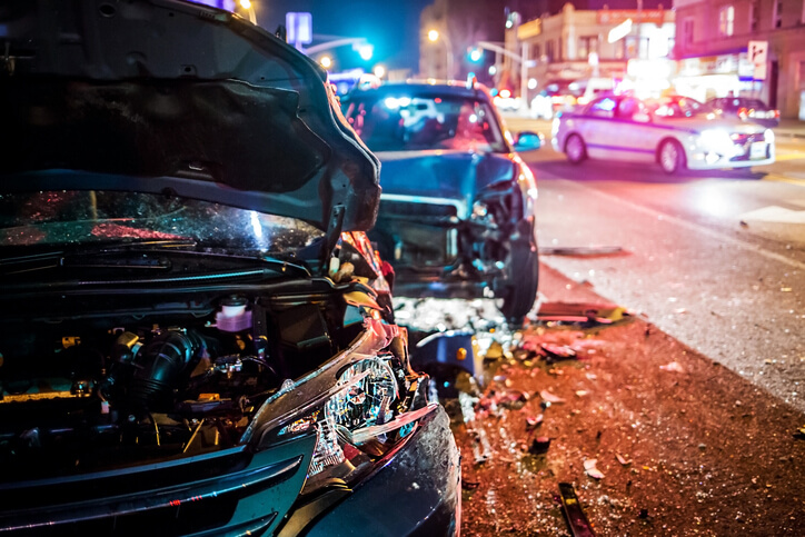 Two vehicles on the side of a busy New York street having just collided with each other. An NY police vehicle looks on, as the owners are thankful they know all the steps to take after an NY car accident.