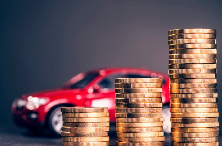 Stacks of coins in the foreground with a sports car in the background illustrating the impact of your vehicle choice on your auto insurance.